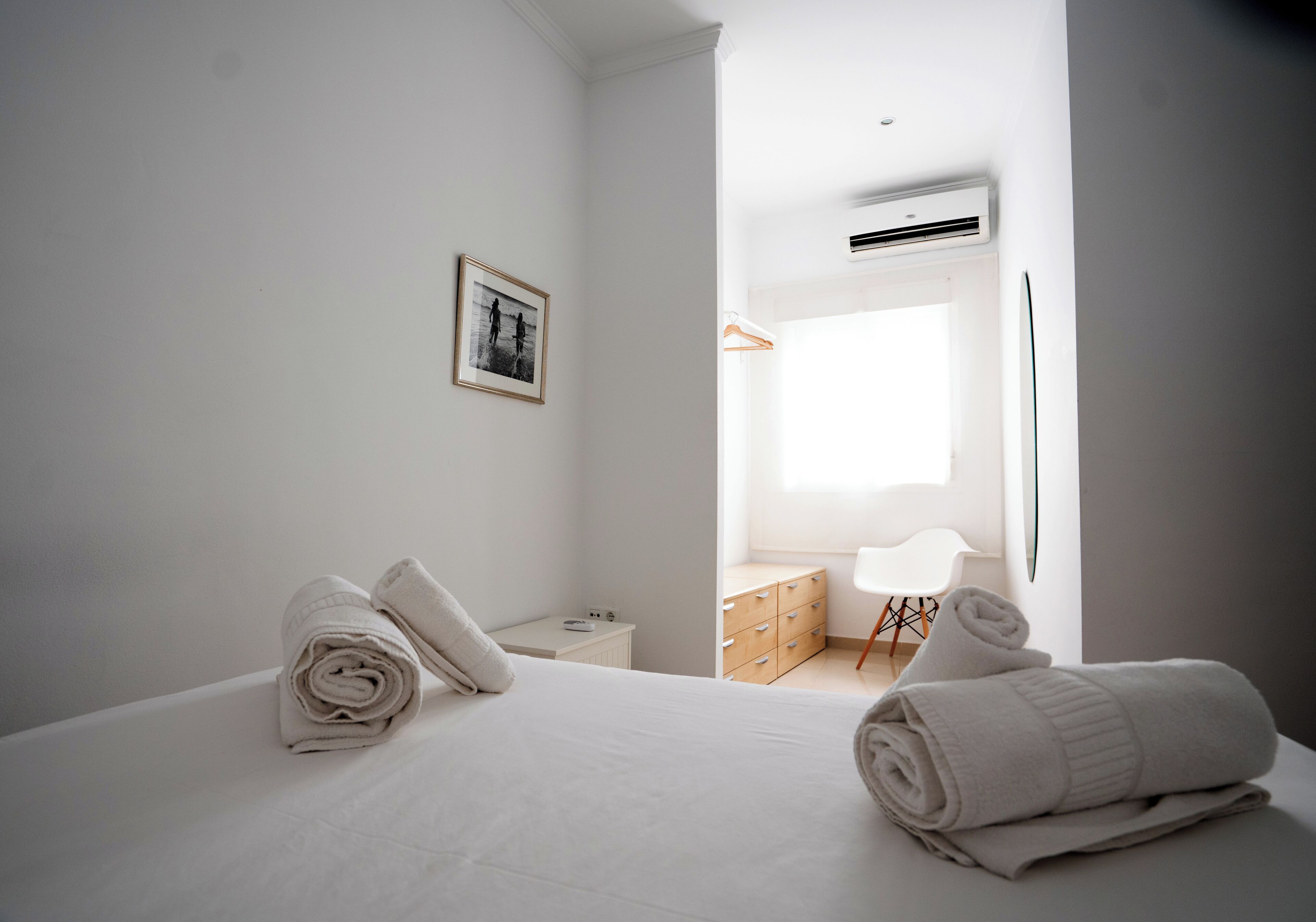 A modern hotel room with a neatly made bed, a bedside table, a dresser, and a chair.