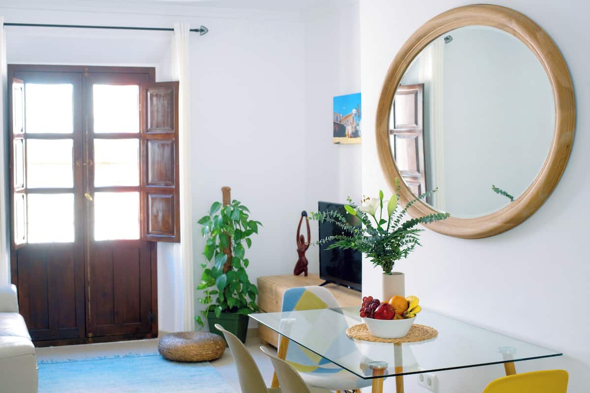 A room with a glass table, a round mirror, a potted plant, and a wooden door.