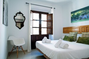 Un dormitorio con cama, una silla, una puerta y un cuadro en la pared.