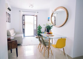 Un comedor moderno con una mesa de vidrio, sillas de madera, una silla amarilla, una planta en maceta y un espejo en la pared.