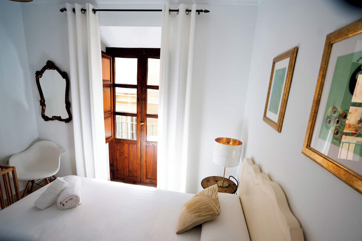 A hotel room with a bed, a chair, a lamp, and a door leading to an outdoor area.