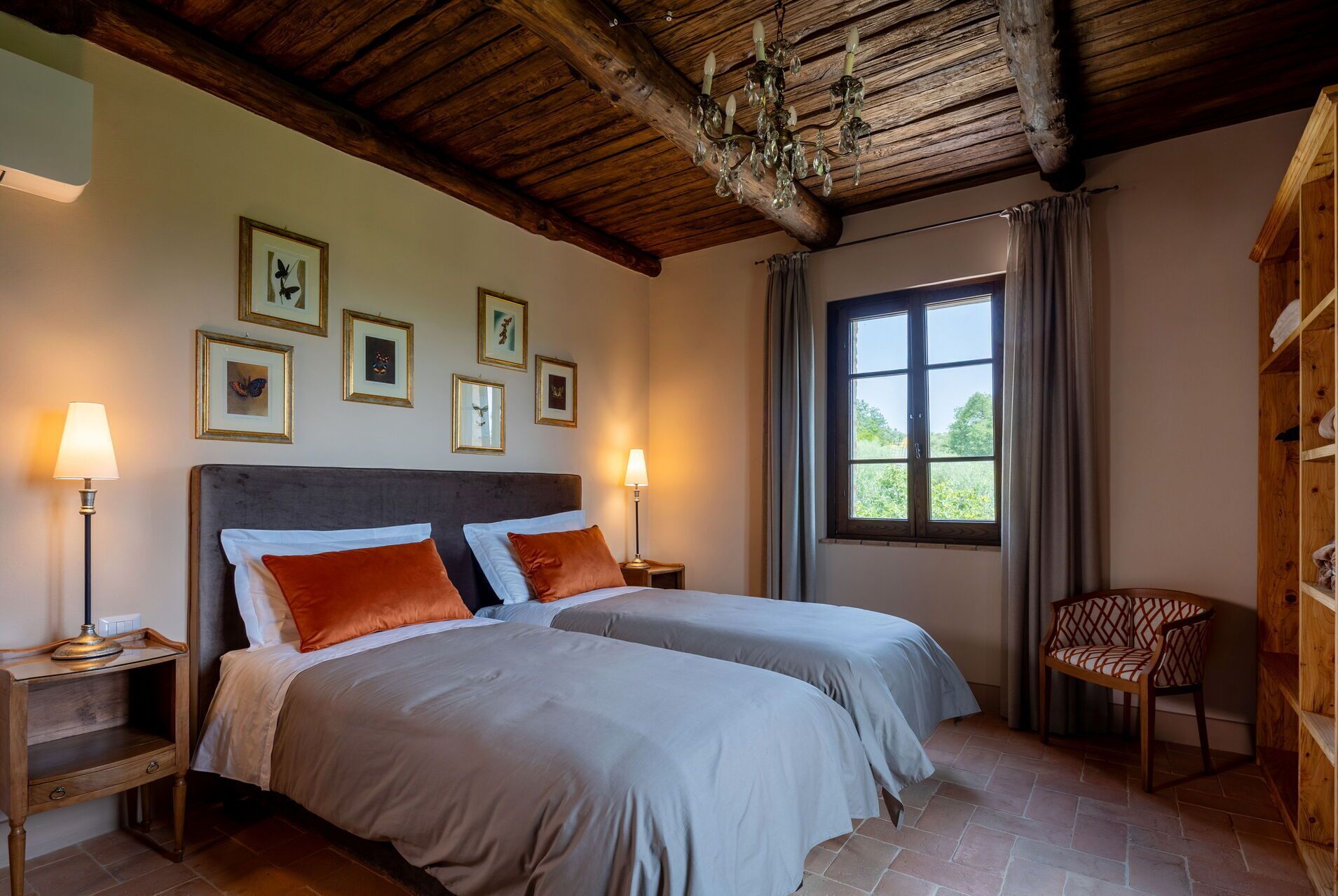 A bedroom with two beds, framed pictures on the wall, a wooden ceiling, and a window with curtains.