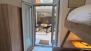 Ein Schlafzimmer mit einem Etagenbett, einem kleinen Tisch und einem Stuhl. Ein Fenster bietet Blick auf einen Innenhof und ein Gebäude.