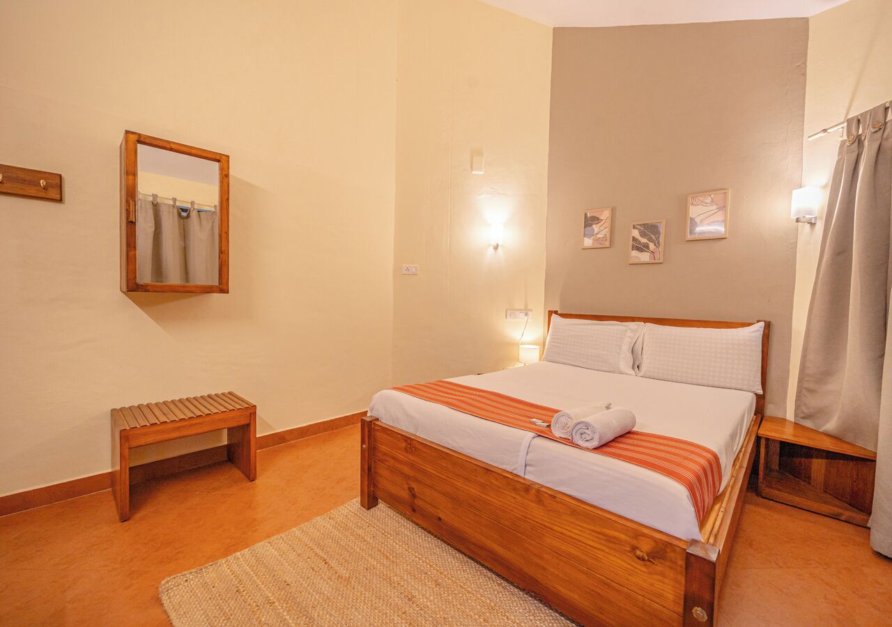 Ein ordentlich eingerichtetes Schlafzimmer mit einem hölzernen Bett, einem kleinen Holzschemel, einem Spiegel und einer Wandleuchte.