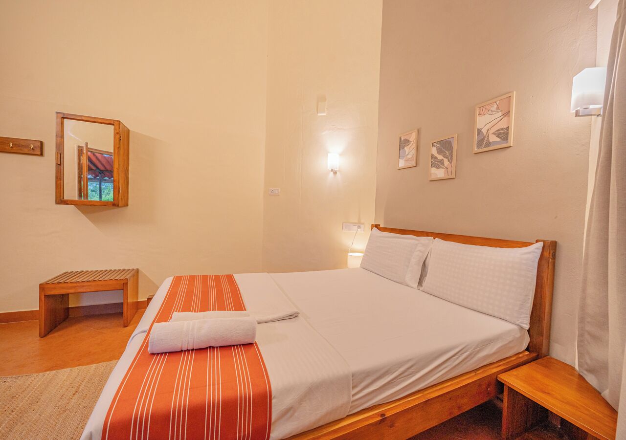 Ein Hotelzimmer mit einem hölzernen Bett, einer kleinen Holzbank, einem wandmontierten Spiegel und einer Wandleuchte.