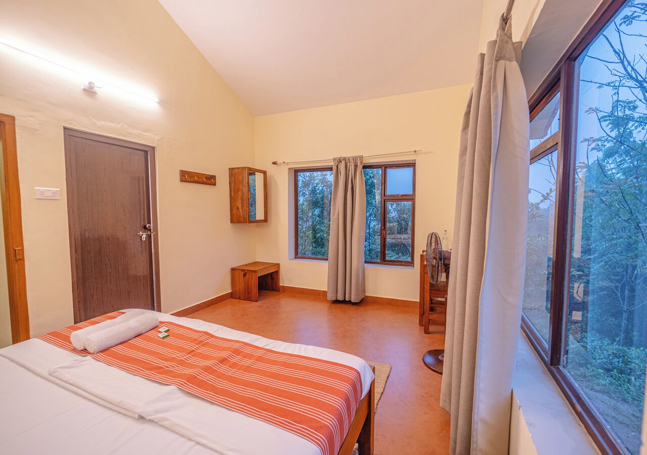 Un dormitorio con cama, un banco de madera, una ventana con cortinas y vista a árboles.