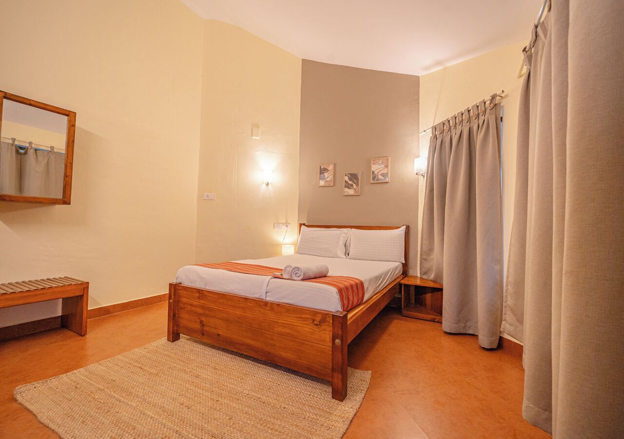 A bedroom with a wooden bed, a bedside table, a bench, and a wall-mounted mirror.