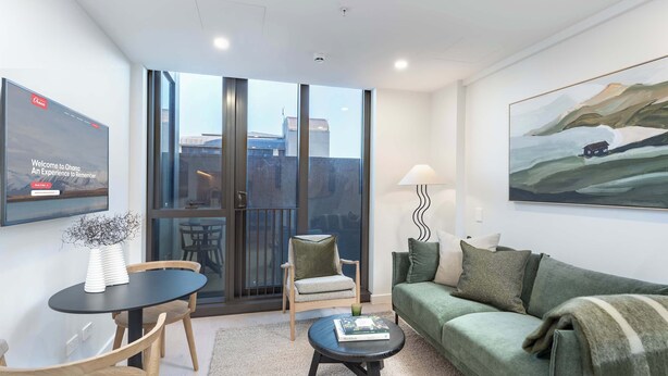 En moderne stue med sofa, sofabord, stol og et fjernsyn ophængt på væggen.