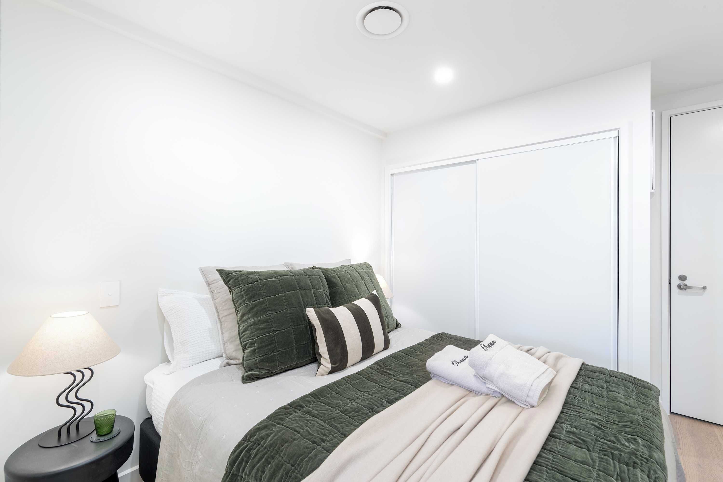 A neatly arranged bedroom with a bed, pillows, a bedside lamp, and a door.