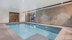 En indendørs swimmingpool med flisegulv og glasafskærmning.