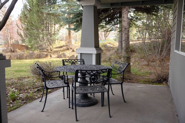 A patio with a round table and four chairs, surrounded by a stone wall and trees. - Rock Bluff Retreat - Home for 6! (Bend)