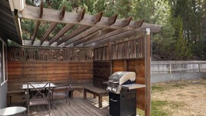 Un patio al aire libre con mesa, sillas y una parrilla de madera.