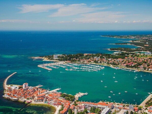 Vista aèria d'una població costanera amb un port esportiu, edificis amb teulades vermelles i aigües blaves cristal·lines.