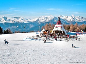 A snow-covered ski slope with a large gathering of people, a ski lift, and a prominent red and white structure in the center. - Beautiful apartment for 3 guests with WIFI, TV and balcony (Veysonnaz)