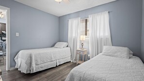 Een slaapkamer met twee eenpersoonsbedden, een nachtkastje met een lamp en een raam met witte gordijnen.