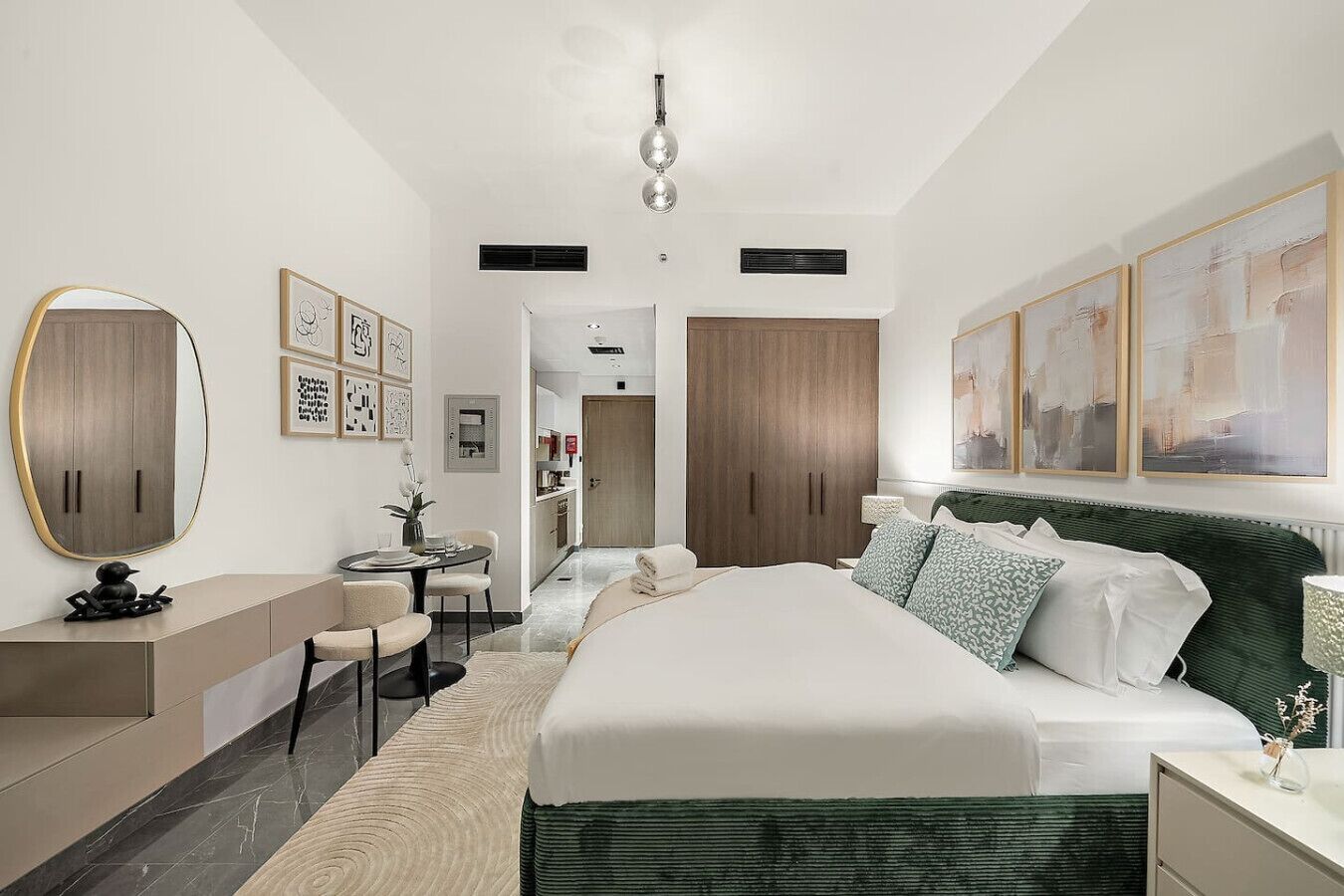 A modern bedroom with a large bed, a desk, and a chair. There is a dining table in the background.