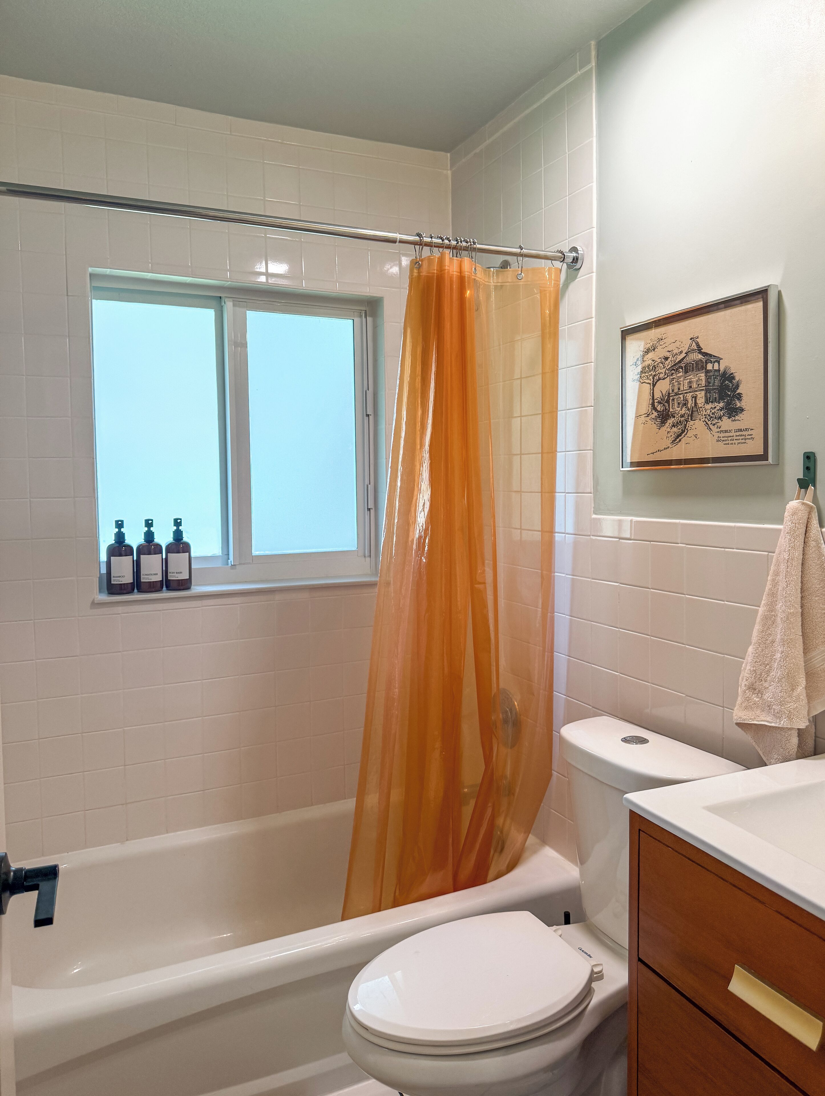 A bathroom with a bathtub, toilet, and window. There are three bottles on the windowsill.
