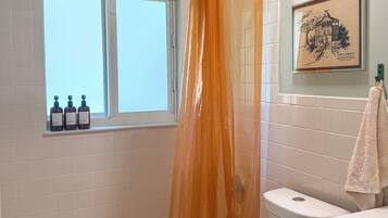 A bathroom with a bathtub, toilet, and window. There are three bottles on the windowsill.