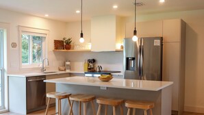 Una cocina moderna con una isla central, electrodomésticos de acero inoxidable, taburetes de madera e iluminación colgante.