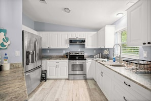 A modern kitchen with stainless steel appliances, white cabinetry, and a granite countertop. - Waterfront home on Spring, Manatees, Boat Slip, Gulf access, scalloping. (Homosassa)