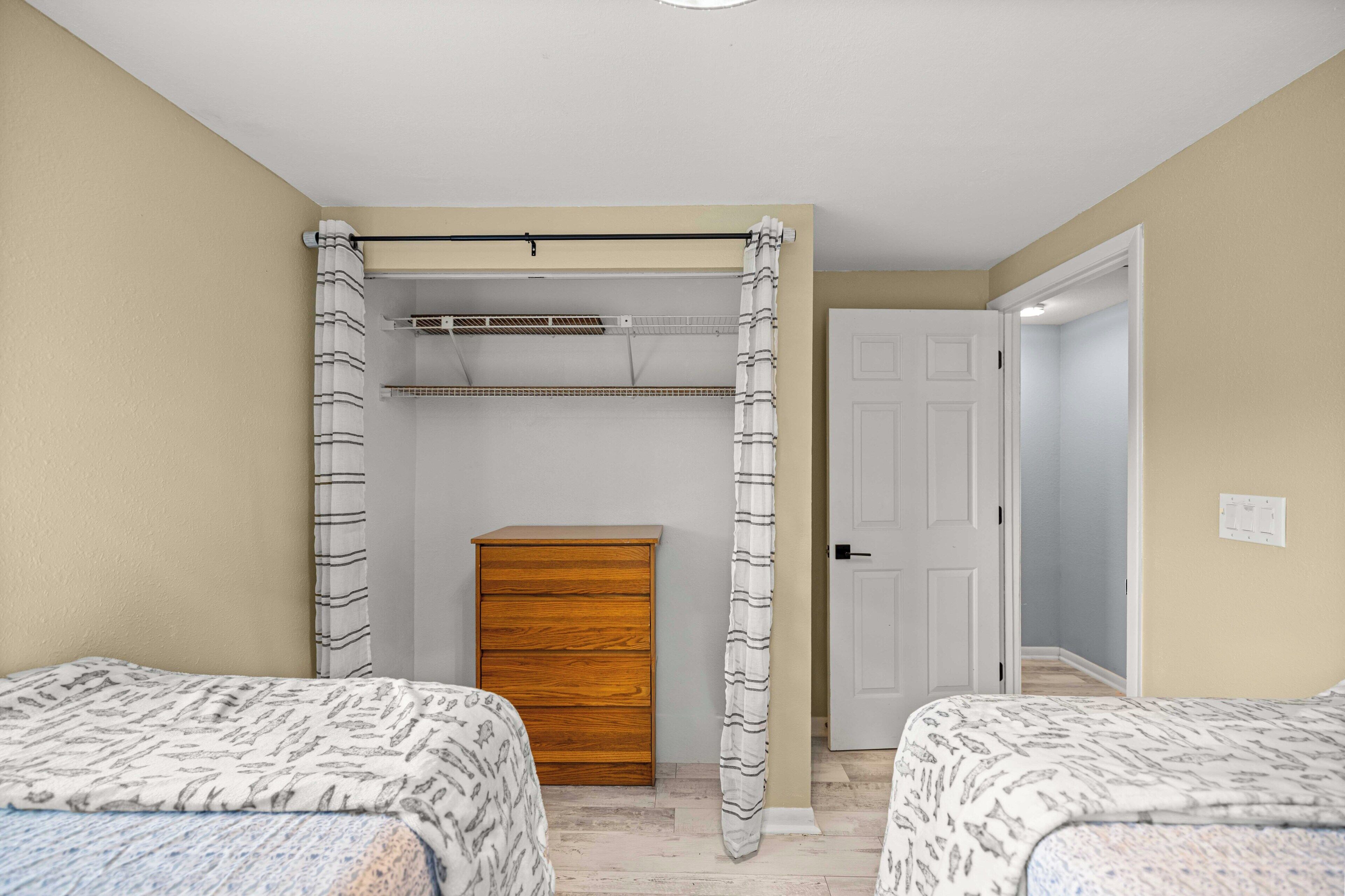 A bedroom with two beds, a wooden dresser, a ceiling fan, and a door leading to another room.