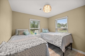 A bedroom with two beds, a ceiling light, and windows with blinds.