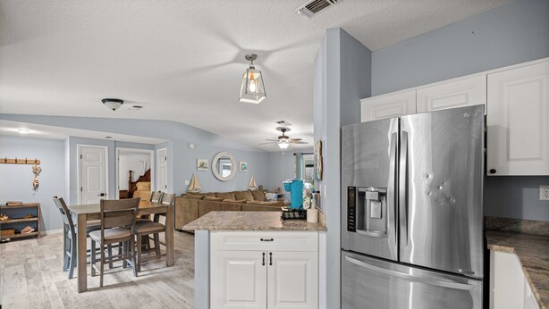 A kitchen with white cabinets, a stainless steel refrigerator, a dining area with a wooden table and chairs, and a ceiling fan. - Waterfront home on Spring, Manatees, Boat Slip, Gulf access, scalloping. (Homosassa)