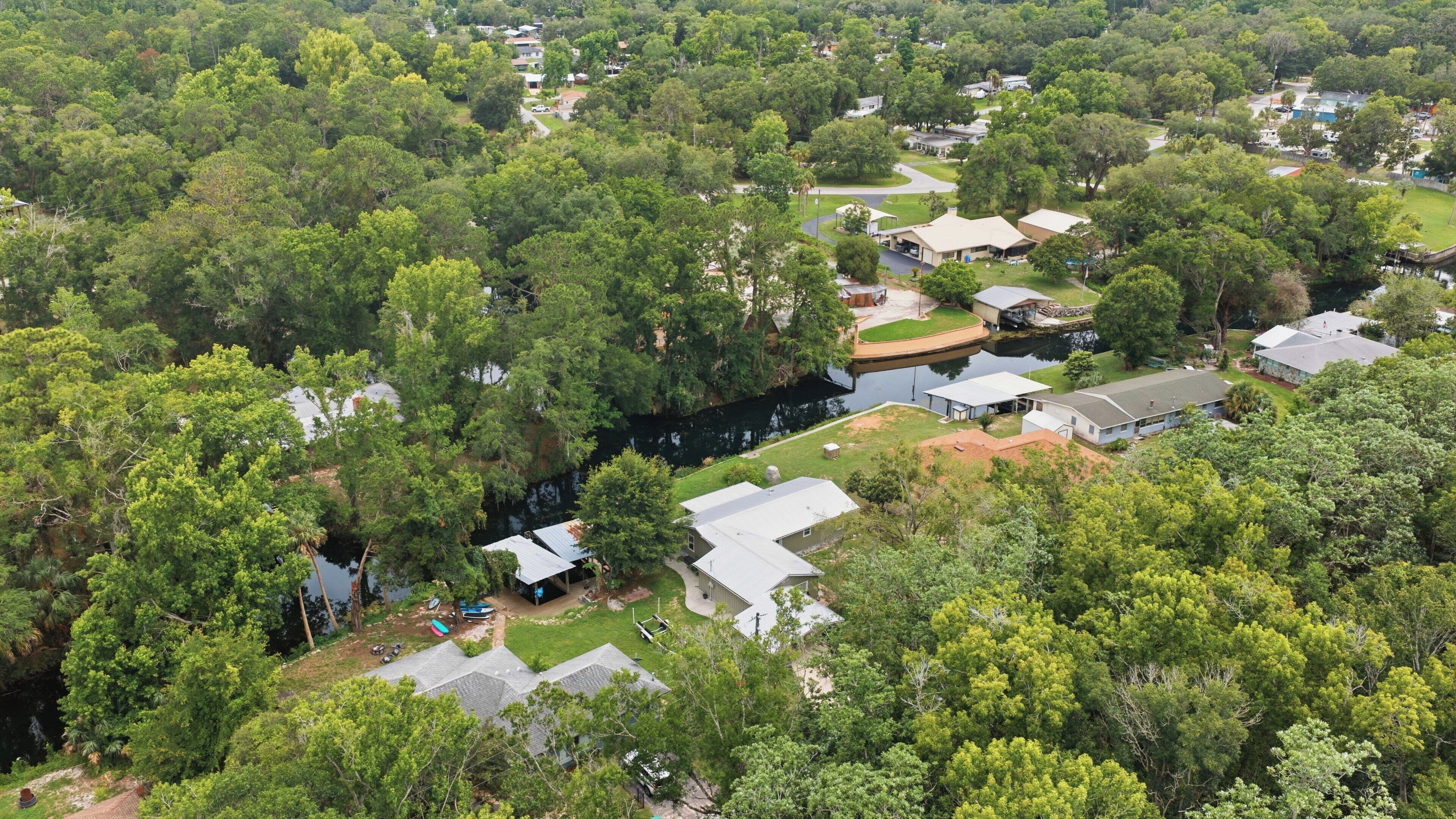 Vue aérienne d’un quartier résidentiel avec des maisons, un étang et une végétation luxuriante.