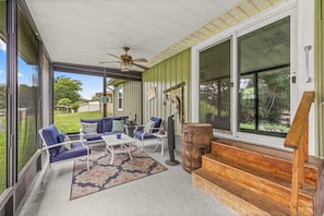 A covered porch with outdoor seating, a wooden barrel, and a staircase leading to a deck.