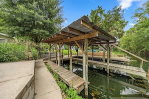 A wooden deck over water with a covered pavilion, surrounded by greenery.