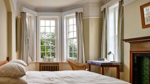 Een slaapkamer met een groot bed, een stoel, een tafel met boeken en een open haard.