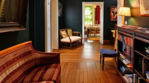 Een kamer met een houten bank, een boekenkast en een zithoek met een tafel en stoelen.