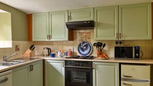 Une cuisine avec des meubles de rangement verts, une cuisinière, un four, un four à micro-ondes et un réfrigérateur.