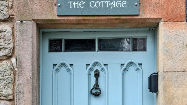 Une porte bleu clair, avec une enseigne au-dessus indiquant « THE COTTAGE ».