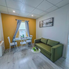 Una sala de estar moderna con un sofá verde, una mesa de comedor con sillas, una mesa de centro y un cuadro en la pared.