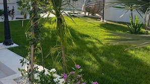 A well-maintained garden with a variety of plants, including a palm tree, flowering shrubs, and a decorative spherical structure in the background. - Dar maryem (Hammam Sousse)
