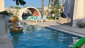 A pool area with lounge chairs, a palm tree, and a clear sky. - Dar maryem (Hammam Sousse)