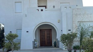 A modern building with a central entrance, a stone wall, and a small balcony. - Dar maryem (Hammam Sousse)
