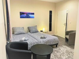 A bedroom with two beds, a desk, a chair, and a painting on the wall.