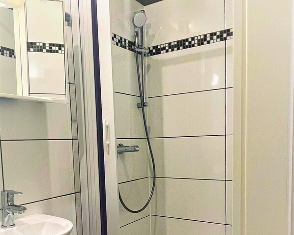 A bathroom with a white sink, a mirror, and a shower with a tiled wall. - Apartment in Pellingen With Parking (Pellingen)