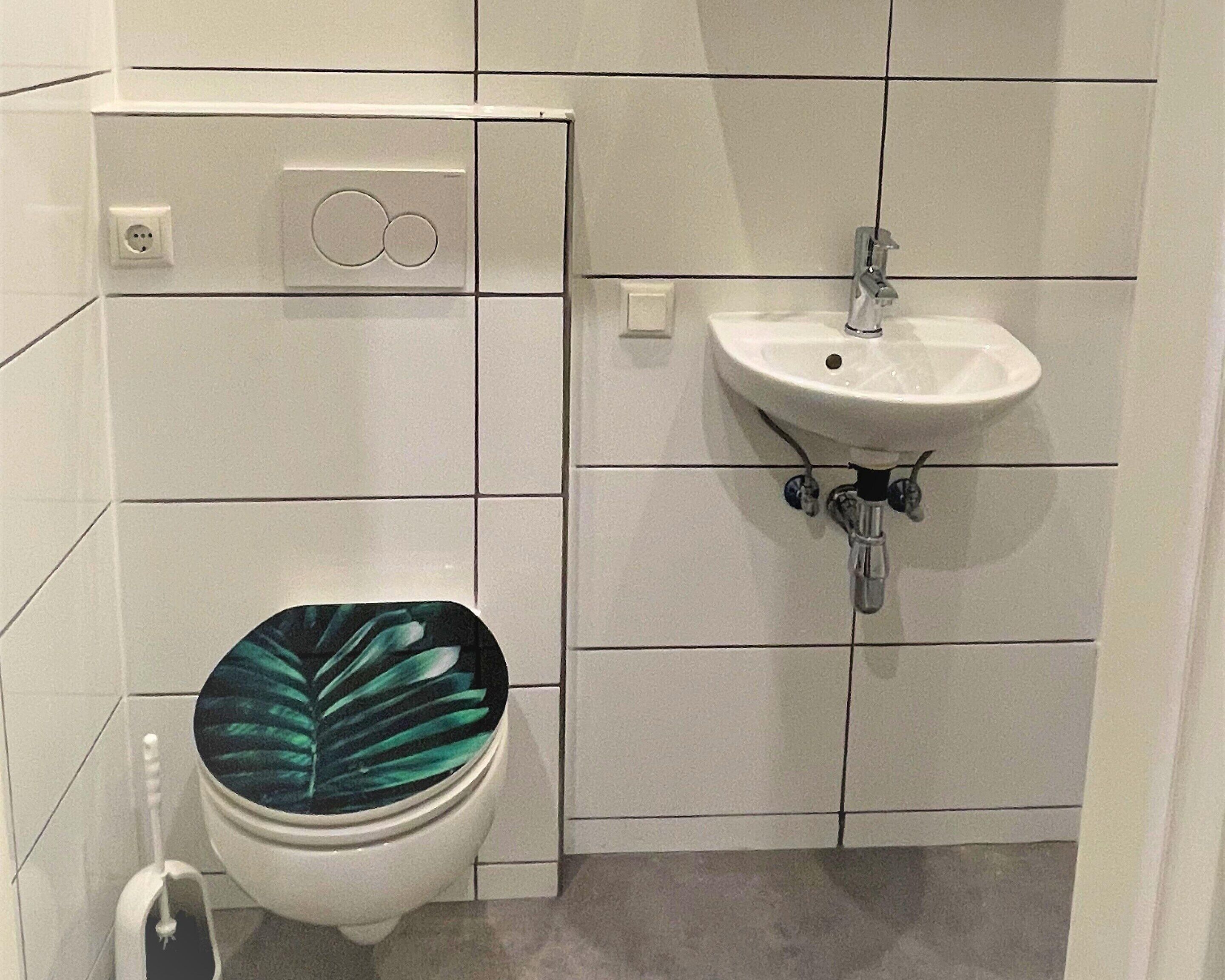 Ein Badezimmer mit Toilette, Waschbecken und einer fest installierten Steckdose.