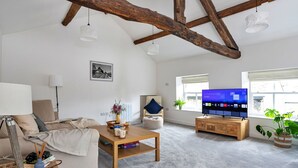 A spacious living room with exposed wooden beams, a television, a sofa, a coffee table, and a bookshelf.