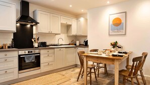 A modern kitchen with white cabinets, a black range hood, and a dining area with a wooden table and chairs.