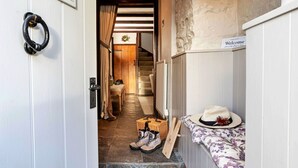 Un estrecho pasillo con una puerta de madera, una escalera y un banco con un sombrero y una cesta.