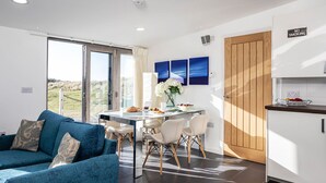 A modern living room with a blue sofa, a dining area with a table and chairs, and a kitchen with a wooden door and a 'No Smoking' sign. - Wonderful  villa for 2 people with WIFI and TV (Barrow In Furness)