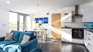 A modern living room with a blue sofa, a dining area with a table and chairs, and a kitchen with white cabinets and a Bosch oven. - Wonderful  villa for 2 people with WIFI and TV (Barrow In Furness)