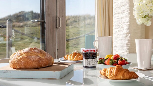 A breakfast setting with croissants, strawberries, a jam jar, and a view of a grassy landscape through a window. - Wonderful  villa for 2 people with WIFI and TV (Barrow In Furness)