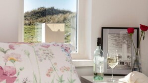 A bedroom with a bed, a window with a view of a hill, a bottle of wine, a glass, and a framed picture on a bedside table. - Wonderful  villa for 2 people with WIFI and TV (Barrow In Furness)