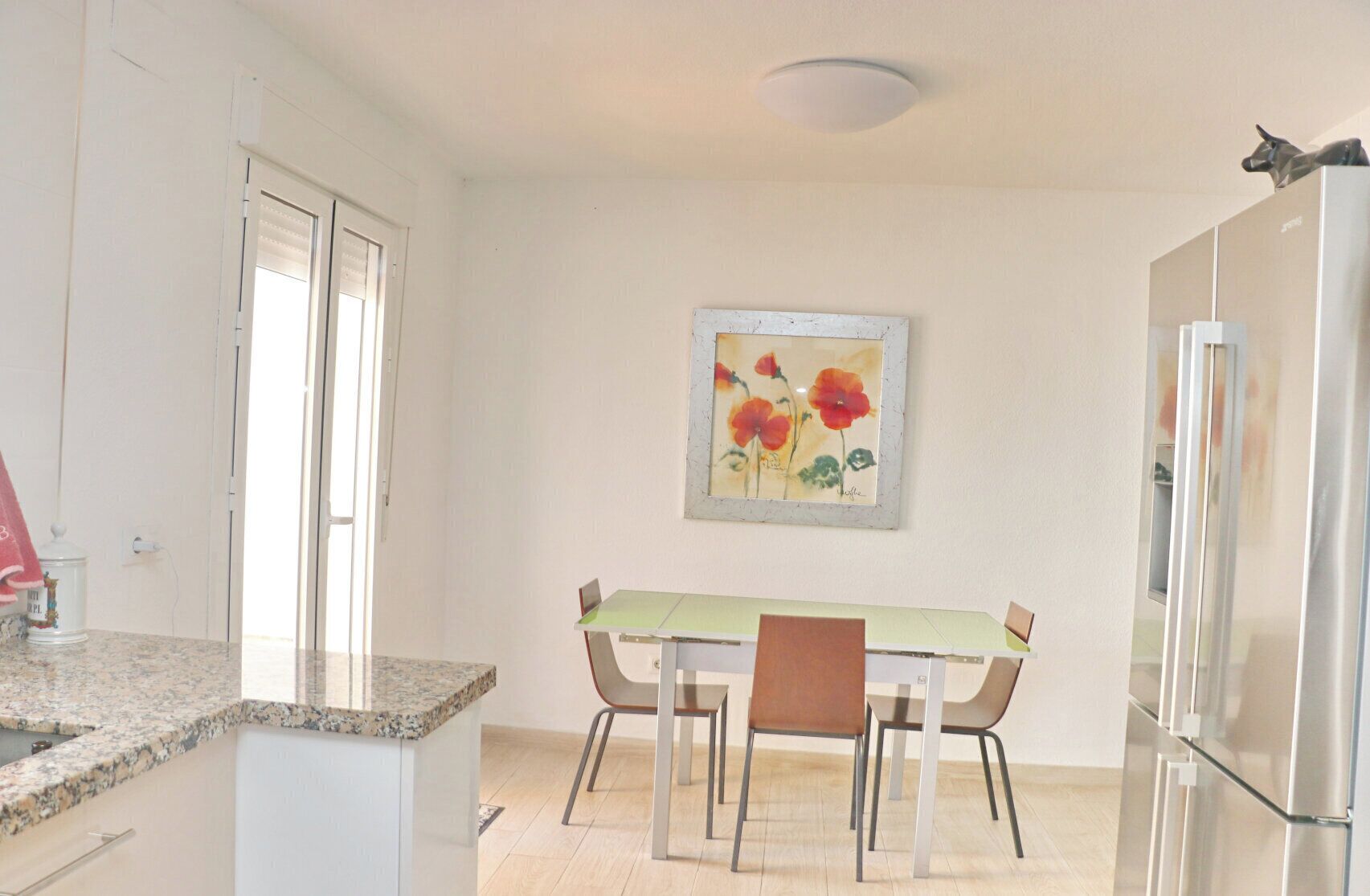 Una cocina con una mesa de comedor, sillas, un refrigerador y un cuadro en la pared.