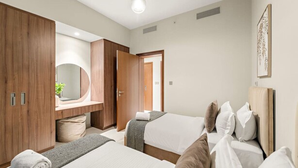 Una camera d'albergo moderna con due letti, un armadio in legno, una toeletta con specchio e un bagno piccolo.